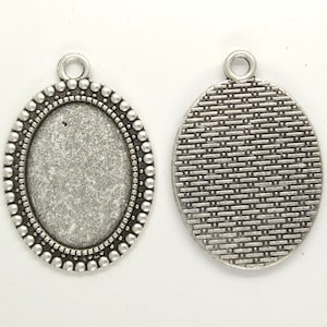 May include: Silver oval pendant with a textured back and a smooth, beveled front. The pendant has a small loop at the top for attaching a chain.