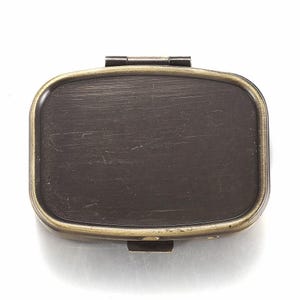 May include: A rectangular, antique-style pillbox with a dark brown interior and a brass-colored frame. The box has a hinged lid and a clasp closure. The surface of the box shows slight wear and tear, giving it a vintage appearance.
