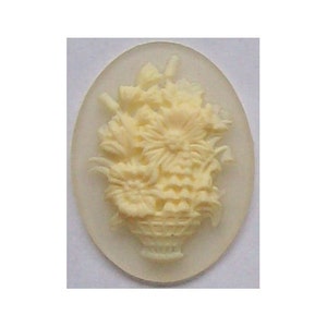 May include: A white cameo with a raised design of a basket of flowers. The cameo is oval shaped and has a smooth, glossy finish.