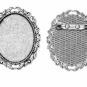 May include: Silver-toned oval-shaped metal brooch with a decorative filigree design. The back of the brooch has a pin and catch closure.