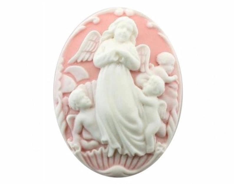 Puede incluir: Un camafeo ovalado rosa con una escultura en relieve blanca de un &aacute;ngel con alas y dos querubines. El &aacute;ngel tiene las manos juntas en oraci&oacute;n.