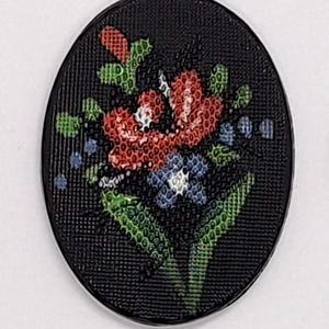 以下が含まれることがあります： 黒い楕円形のボタン、花の模様。 ボタンは、テクスチャ加工された表面と、赤、青、緑の花のカラフルな刺繍ブーケが特徴です。 ボタンはおそらく縫製や工芸品用です。