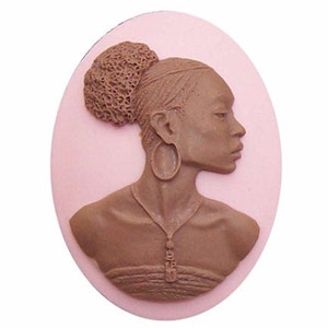 May include: A brown cameo featuring a woman with a brown bun, large hoop earrings, and a necklace. The cameo is set against a pink background.