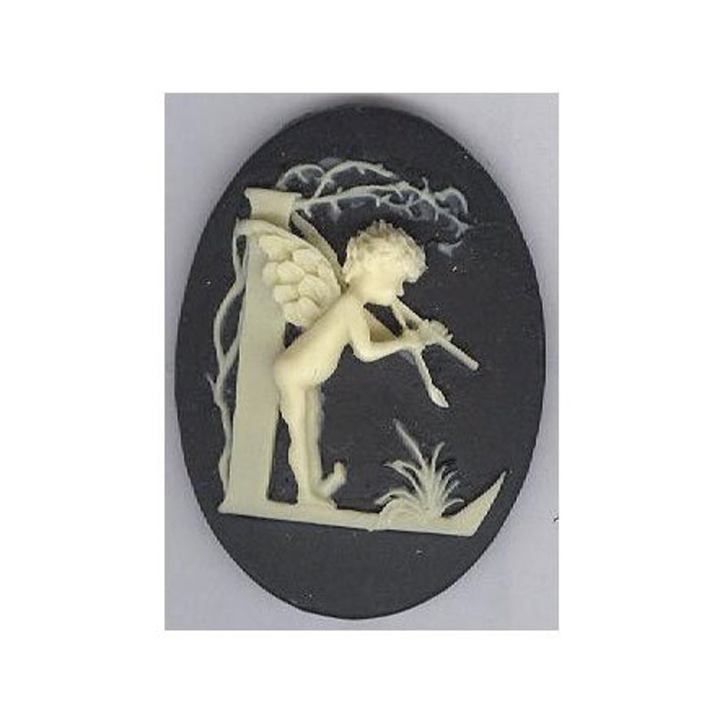 May include: Oval cameo pendant featuring a cream-colored cherub playing a flute, set against a dark gray background. The cherub is positioned near a tree and grass, with intricate details. The pendant is likely made of ceramic or a similar material.