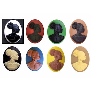 May include: Set of eight oval-shaped cameo-style buttons featuring a profile of a woman with a bun hairstyle. The buttons are in various colors, including black, white, red, green, blue, yellow, brown, and beige.