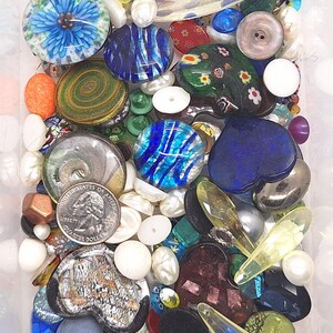以下が含まれることがあります： カラフルなガラスビーズ、ボタン、装飾要素のコレクション。青、緑、透明なガラス片、白い真珠、硬貨が含まれています。さまざまな形とサイズがあり、多様な組み合わせを作り出しています。