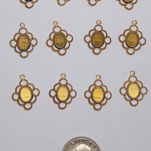 May include: Twelve gold-toned metal pendant frames with a decorative oval design. Each frame has a small loop at the top for attaching a chain or cord. The frames are approximately the size of a US quarter.