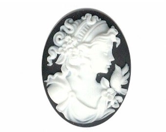 May include: White cameo with a woman's profile wearing a crown and holding a bird. The cameo is set in a black oval frame.