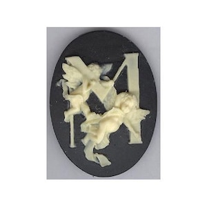 May include: A black cameo with a white cherub design. The cherub is holding a cross and is surrounded by a white letter "M".