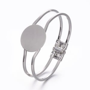 May include: Silver bangle bracelet with a round, smooth, silver disc in the center. The bracelet has a hinged clasp.