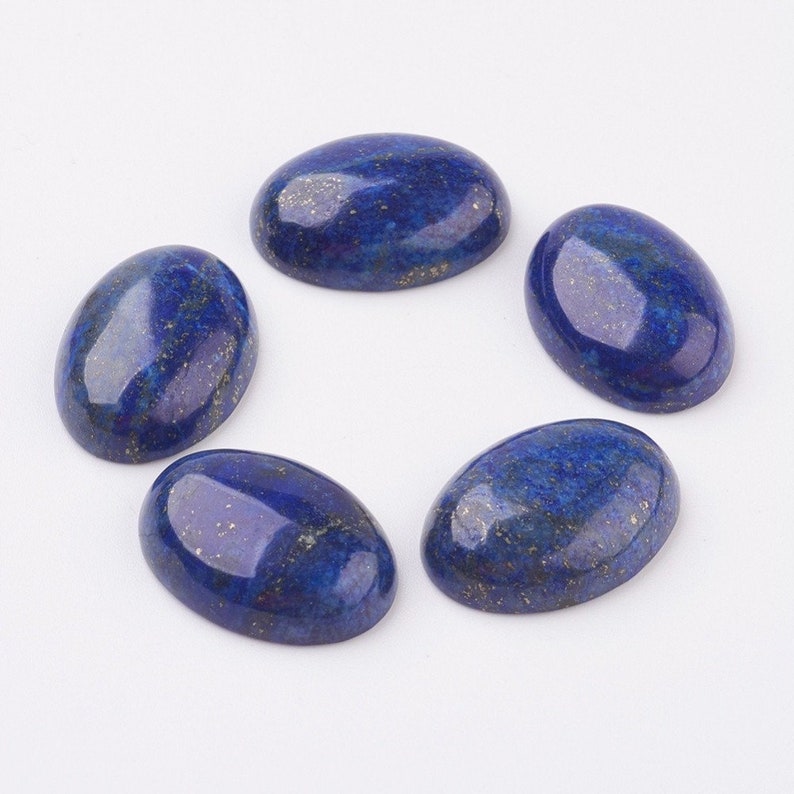 Pode incluir: Cinco pedras preciosas ovais de l&aacute;pis-laz&uacute;li. As pedras s&atilde;o de cor azul profundo com manchas douradas. As pedras est&atilde;o dispostas em um padr&atilde;o circular sobre um fundo branco. Ideais para a cria&ccedil;&atilde;o de joias.