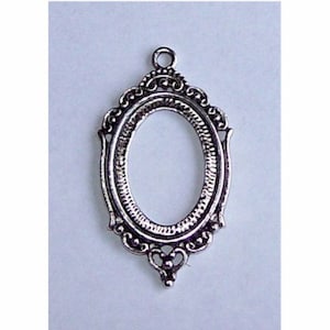 May include: Silver oval-shaped pendant with an ornate frame. The frame has a detailed design with a loop at the top for hanging.