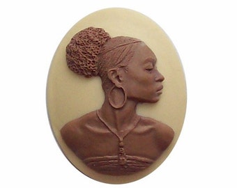 May include: A brown cameo featuring a woman with a brown bun hairstyle and large hoop earrings. The cameo is set against a cream background.