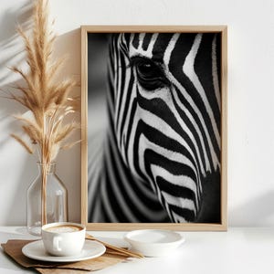 May include: A framed black and white photograph featuring a close-up of a zebra's eye and facial stripes. The rectangular print is encased in a light-toned wooden frame, showcasing the high-contrast pattern of the animal's fur in sharp detail.