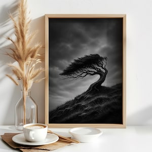 May include: A framed black and white wall art print depicting a solitary tree bent by the wind on a grassy hill under a cloudy sky. Next to the frame is a clear glass vase with dried pampas grass, a white coffee cup on a saucer, and a small bowl.