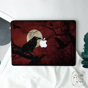 May include: A laptop case featuring a dark, gothic design. A black raven perches on a tree branch against a red background with a full moon. Silhouetted trees and flying ravens complete the spooky scene. The Apple logo is visible.