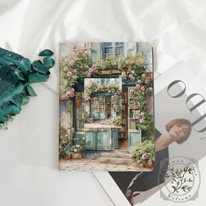 May include: A notebook with a watercolor illustration of a bookstore facade, adorned with pink roses and greenery. The image features a small inset of the same scene, creating a layered effect. The notebook is on a white surface.