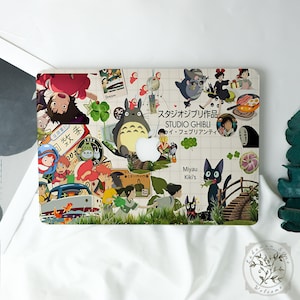 May include: A laptop case featuring a collage of Studio Ghibli characters and imagery. The design includes characters from various Ghibli films, with Japanese text and a white background. The case has a cutout for the Apple logo.