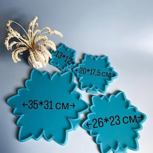 Pu&ograve; includere: Quattro vassoi turchesi a forma di fiore di varie dimensioni. Le misure sono indicate su ogni vassoio: 13x12 cm, 20x17,5 cm, 35x31 cm e 26x23 cm. Un vaso con spighe di grano secche sullo sfondo.
