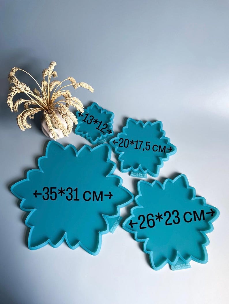 Pu&ograve; includere: Quattro vassoi turchesi a forma di fiore di varie dimensioni. Le misure sono indicate su ogni vassoio: 13x12 cm, 20x17,5 cm, 35x31 cm e 26x23 cm. Un vaso con spighe di grano secche sullo sfondo.