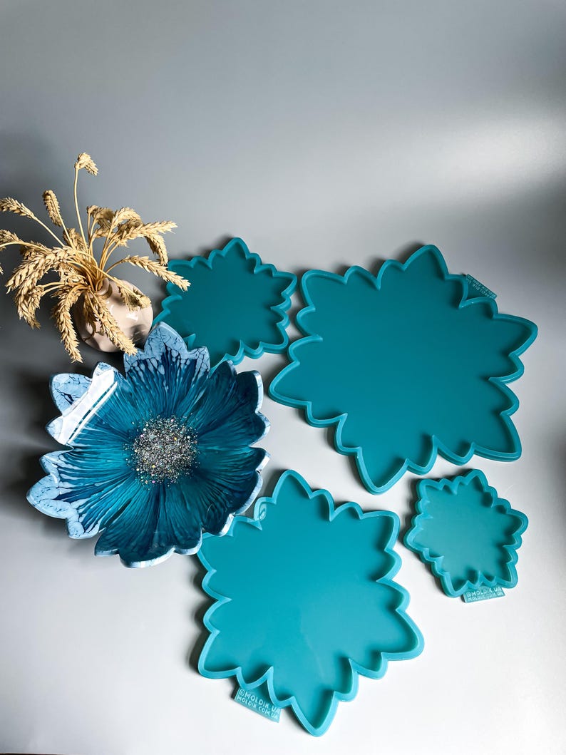 Pu&ograve; includere: Una collezione di stampi in resina turchese a forma di fiore di varie dimensioni, insieme a una ciotola di fiori in resina finita con un design marmorizzato blu e bianco e un centro glitterato argentato. &Egrave; presente anche un piccolo vaso con grano secco.