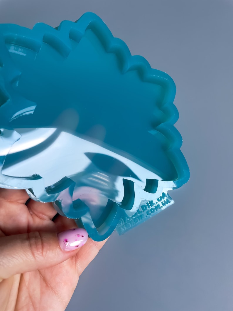 Pu&ograve; includere: Uno stampo in silicone traslucido color turchese a forma floreale. Lo stampo &egrave; tenuto in una mano con una manicure rosa chiaro. Lo stampo ha una superficie liscia e lucida ed &egrave; progettato per l'artigianato.