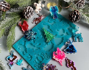 Può includere: Una collezione di ornamenti natalizi colorati e glitterati, tra cui angeli, fiocchi di neve e renne, insieme a uno stampo in silicone turchese. Gli ornamenti sono di varie forme e colori, con un tema festivo. Pigne e rami di pino completano l'arredamento natalizio.