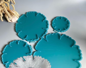 Può includere: Una collezione di vassoi e sottobicchieri in resina a forma di fiore, color turchese. Il set include varie dimensioni, con una ciotola trasparente a forma di fiore in primo piano. Tema di arredamento per la casa.