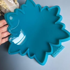Pu&ograve; includere: Uno stampo in silicone a forma di fiore, di colore turchese brillante. Lo stampo ha una finitura lucida e un bordo smerlato dettagliato. Il testo "@MOLDIK.UA MOLDIK.COM.UA" &egrave; visibile in basso a destra. Progettato per l'artigianato.