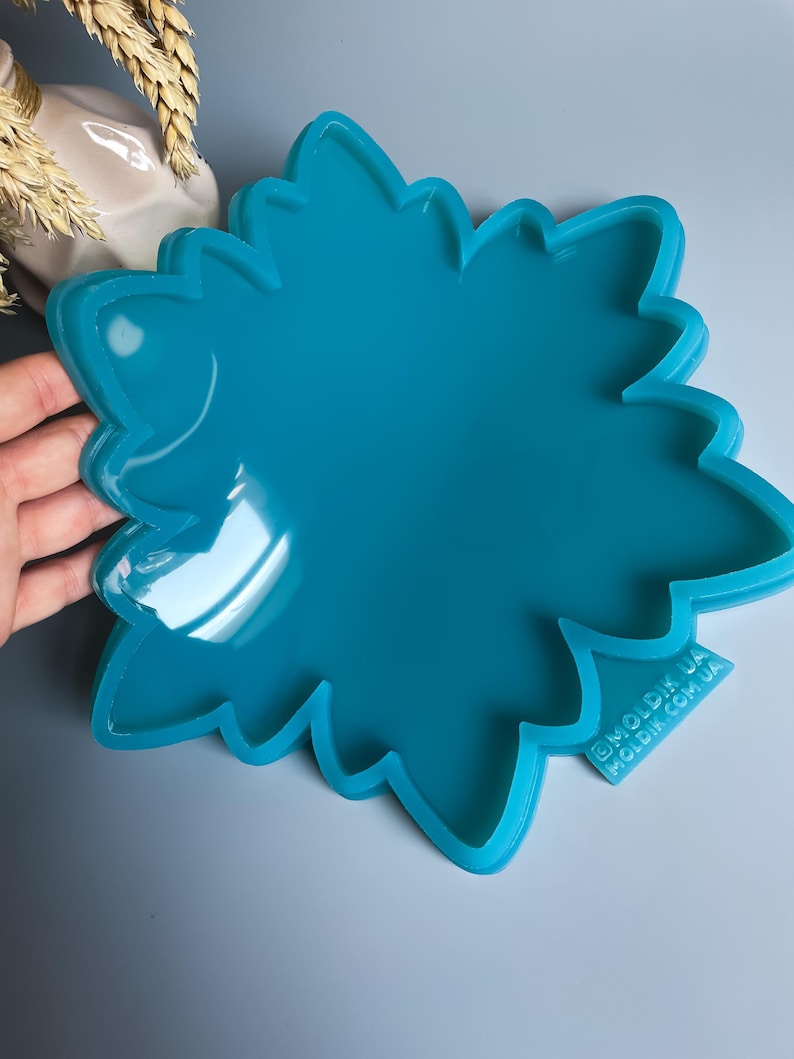 Pu&ograve; includere: Uno stampo in silicone a forma di fiore, di colore turchese brillante. Lo stampo ha una finitura lucida e un bordo smerlato dettagliato. Il testo "@MOLDIK.UA MOLDIK.COM.UA" &egrave; visibile in basso a destra. Progettato per l'artigianato.