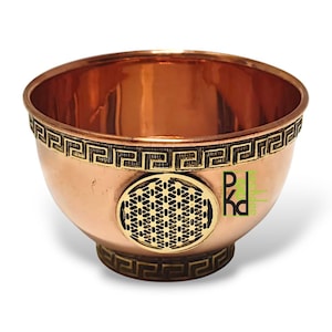 Könnte beinhalten: Eine kupferfarbene Schale mit einem dekorativen griechischen Schlüsselmuster am Rand und am Boden. Ein kreisförmiges, goldfarbenes Design befindet sich in der Mitte der Schale. Die Schale hat ein poliertes, reflektierendes Innere.