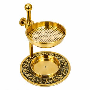Puede incluir: Un quemador de incienso de metal dorado con una base circular con patrones florales en relieve, un pilar central con una perilla de ajuste de altura y un cuenco perforado superior, todo con un acabado en tono metálico pulido.