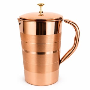 Puede incluir: Una jarra de cobre con acabado pulido y tapa a juego que presenta un pequeño pomo de tono dorado. El cuerpo de la jarra muestra bandas alternas de cobre liso y reflectante junto a franjas de cobre cepillado con textura mate.