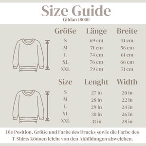 May include: A Gildan 18000 size guide chart featuring two line-art illustrations of a crewneck sweatshirt. The chart displays measurements in both centimetres and inches for sizes S, M, L, XL, and XXL, detailing length and width dimensions.