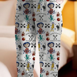 May include: White pajama trousers featuring a repeating pattern of cartoon characters, text, and symbols. The design includes a girl with blue hair, a black cat, and the words "Pink Palace" and "Be Brave".