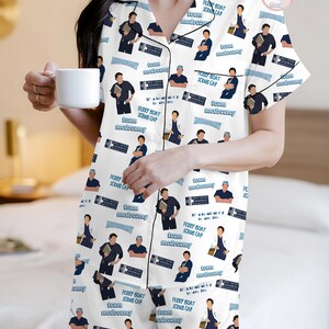 May include: White pajama set with a black trim, featuring a repeating pattern of illustrations and text. The design includes images of a man in various poses, along with the phrases "Ferry Boat Scrub Cap", "Team Medreamy", and "Grey Sloan Memorial Hospital".