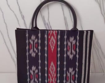 May include: A black tote bag with a patterned design in red, white, and navy blue. The bag has a rectangular shape with a dark brown handle. The text "MaulidiaGifts" is at the bottom right.