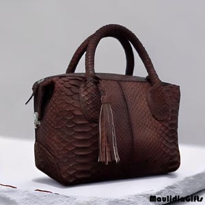 May include: A brown leather handbag with a textured snakeskin pattern. The bag has two braided handles and a decorative tassel. The bag has a rectangular shape and a zipper closure. The bag is sitting on a white surface.
