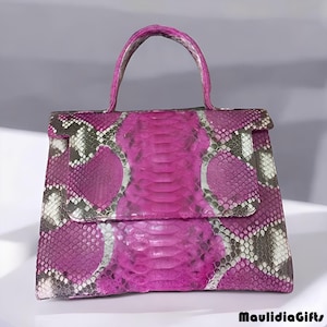 May include: A magenta handbag with a top handle and a flap closure. The bag is made of snakeskin with a pattern of magenta, gray, and white scales. The brand name "MaulidiaGifts" is printed in black at the bottom right.