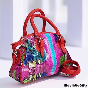 May include: A colorful handbag with a snakeskin pattern in shades of pink, blue, green, and yellow. The bag has red handles and a red shoulder strap. The bag is a medium size.