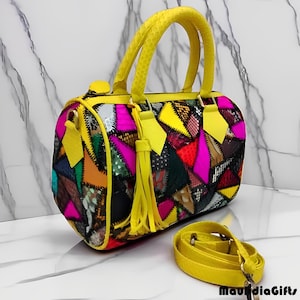 May include: A colorful patchwork handbag with yellow handles and a detachable shoulder strap. The bag features a variety of geometric shapes in shades of pink, yellow, green, and blue. A yellow tassel hangs from the side.