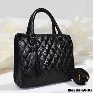 May include: Black handbag with a quilted pattern and a top handle. The bag has a detachable shoulder strap and a decorative tassel. The bag is made of a textured material and has gold-colored hardware.
