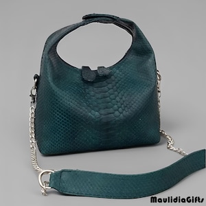 May include: Teal green handbag with a snakeskin pattern. The bag has a curved top handle and a detachable silver chain strap. The bag is approximately 10 inches wide and 8 inches tall.