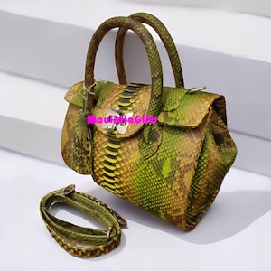 May include: A green and yellow snakeskin handbag with a matching shoulder strap. The bag has a top handle and a silver clasp closure. The bag has a tassel and the text "MauiiaGifts".