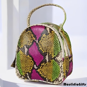 May include: A small, colorful backpack with a snakeskin pattern. The bag features a handle and a zipper closure. The pattern includes shades of green, yellow, pink, and brown. The bag is made of a textured material.