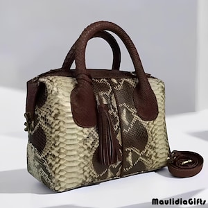 May include: A rectangular handbag with a snakeskin pattern in shades of brown, beige, and black. The bag features two top handles and a detachable shoulder strap. A brown tassel hangs from the side. The bag is a stylish accessory.