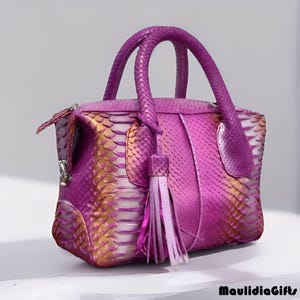 May include: A vibrant, textured handbag in shades of pink and gold, featuring a snakeskin pattern. The bag has a top handle, a zipper closure, and a decorative tassel. The brand name "MaulidiaGifts" is visible.