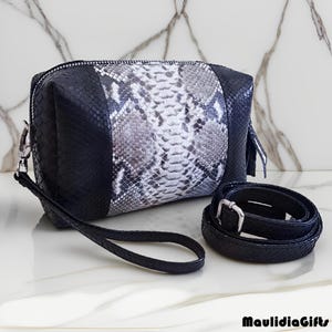 May include: A black and silver snakeskin-patterned clutch with a matching strap and a detachable shoulder strap. The clutch has a zipper closure and silver-tone hardware. The bag is rectangular and has a wrist strap.