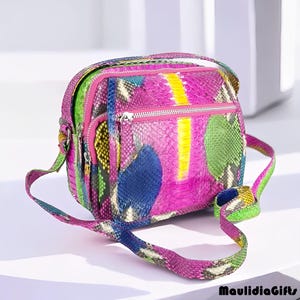 May include: A colorful crossbody bag with a vibrant snakeskin pattern. The bag features a mix of pink, blue, green, and yellow hues, with a zippered main compartment and a long strap. The bag is a stylish accessory.