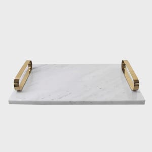 May include: A rectangular white marble serving tray featuring a polished surface with subtle grey veining. The tray is equipped with two smooth, curved gold-toned metal handles attached to the shorter sides, providing a functional grip for transport.